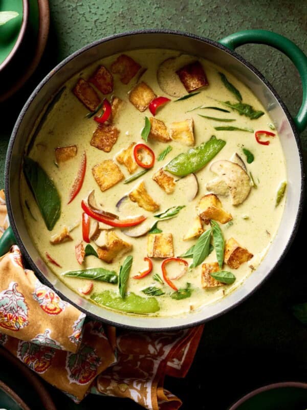 vegan thai green curry with vegetables and crispy tofu in a green saucepan on a green table.