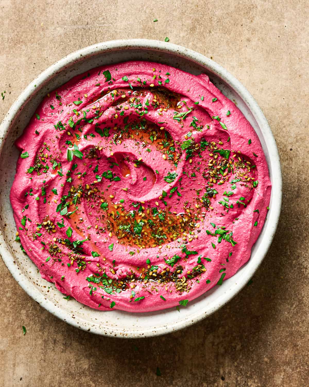 Large shallow bowl of beet hummus with parsley and oil on a table.