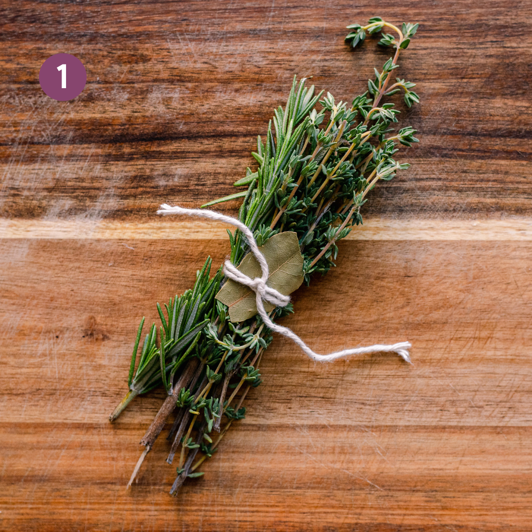 a bouquet garni or bundle of fresh rosemary, thyme, and bay leaves tied together with kitchen twine on a wooden cutting board.