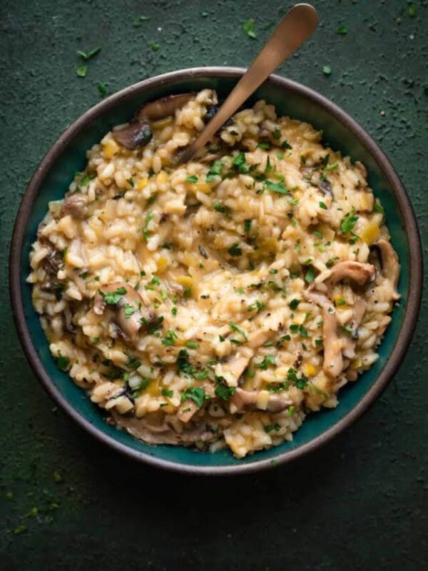 creamy, velvety vegan mushroom risotto in a green bowl with spoon dug in on a dark green table.