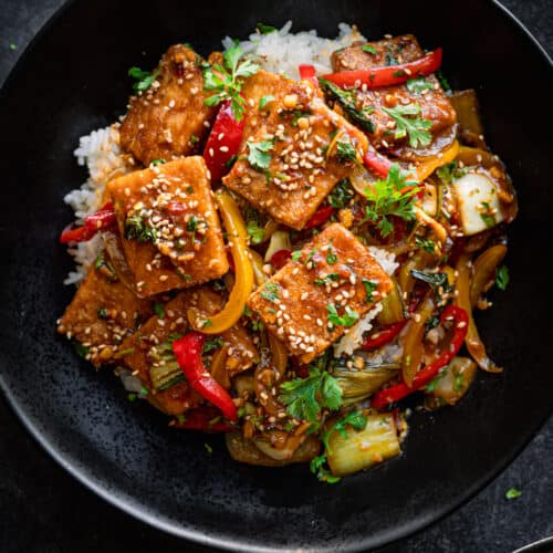 Tofu and pepper stir fry on a bed of white rice in a black bowl.