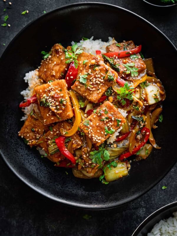 Tofu and pepper stir fry on a bed of white rice in a black bowl.