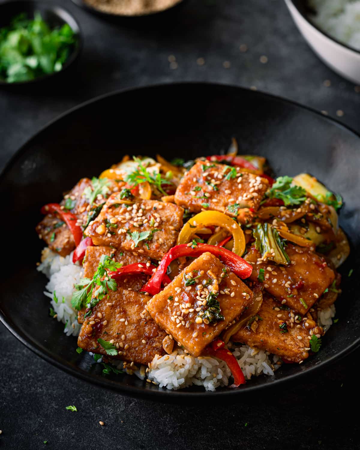 Finished tofu with peppers on a bed of white rice in a black bowl.