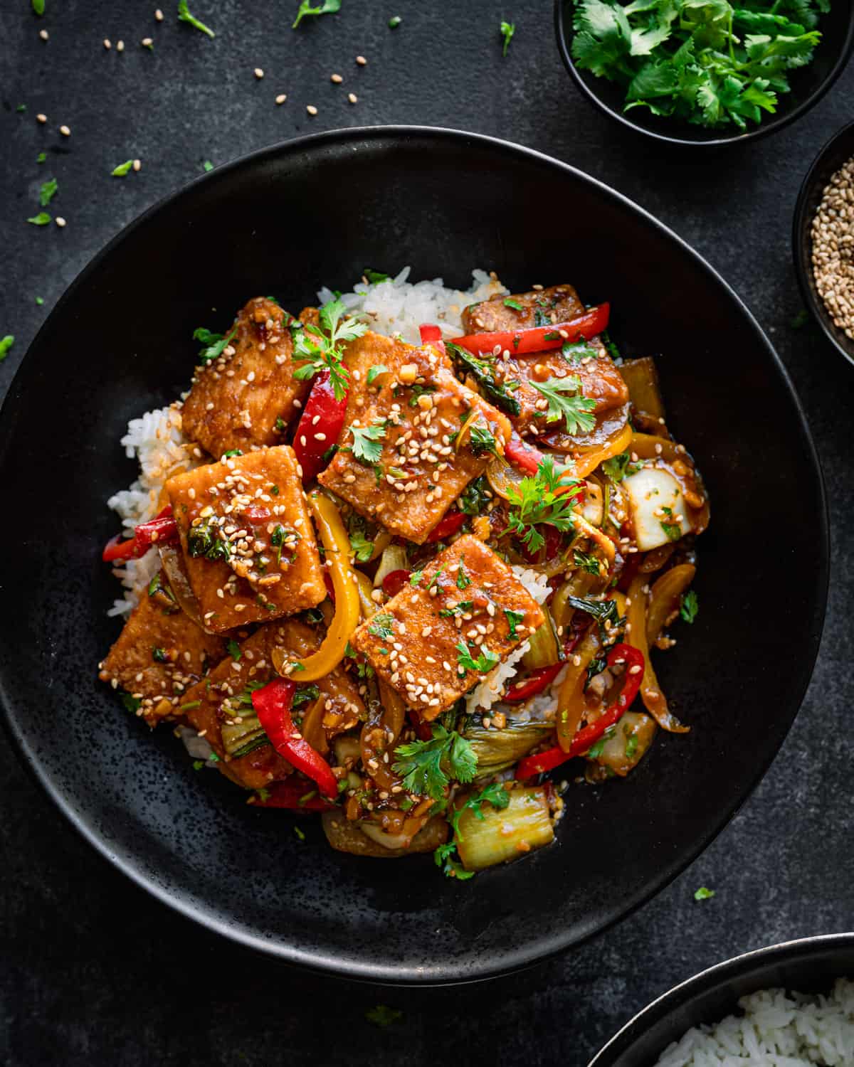Tofu and pepper stir fry on a bed of white rice in a black bowl.