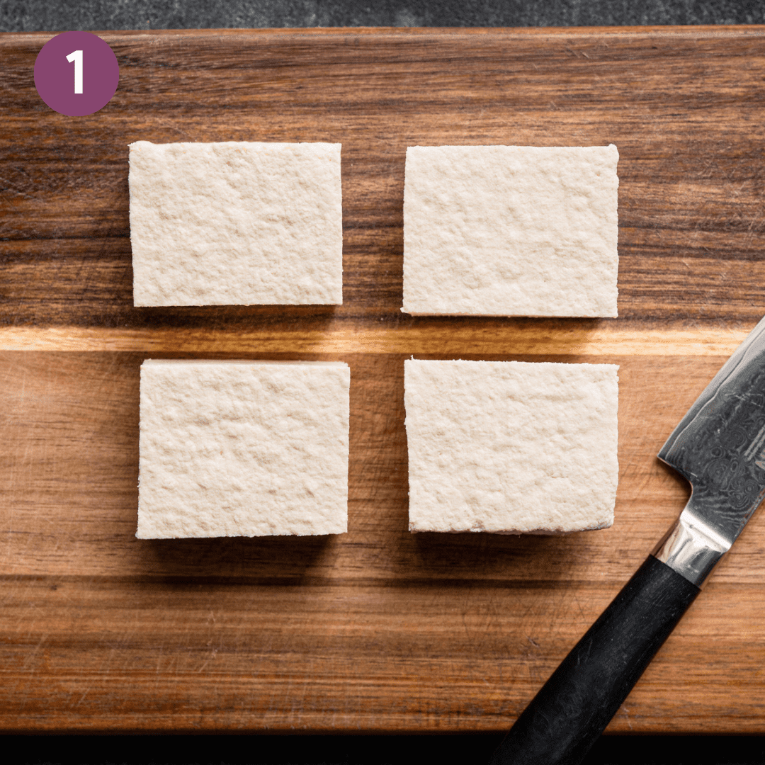 Tofu slabs cut into squares on wooden cutting board.
