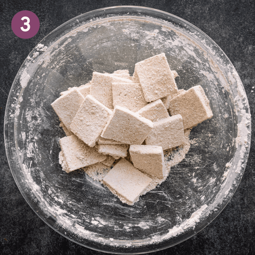 Tofu cut into squares covered in cornstarch and spices in a large glass bowl.