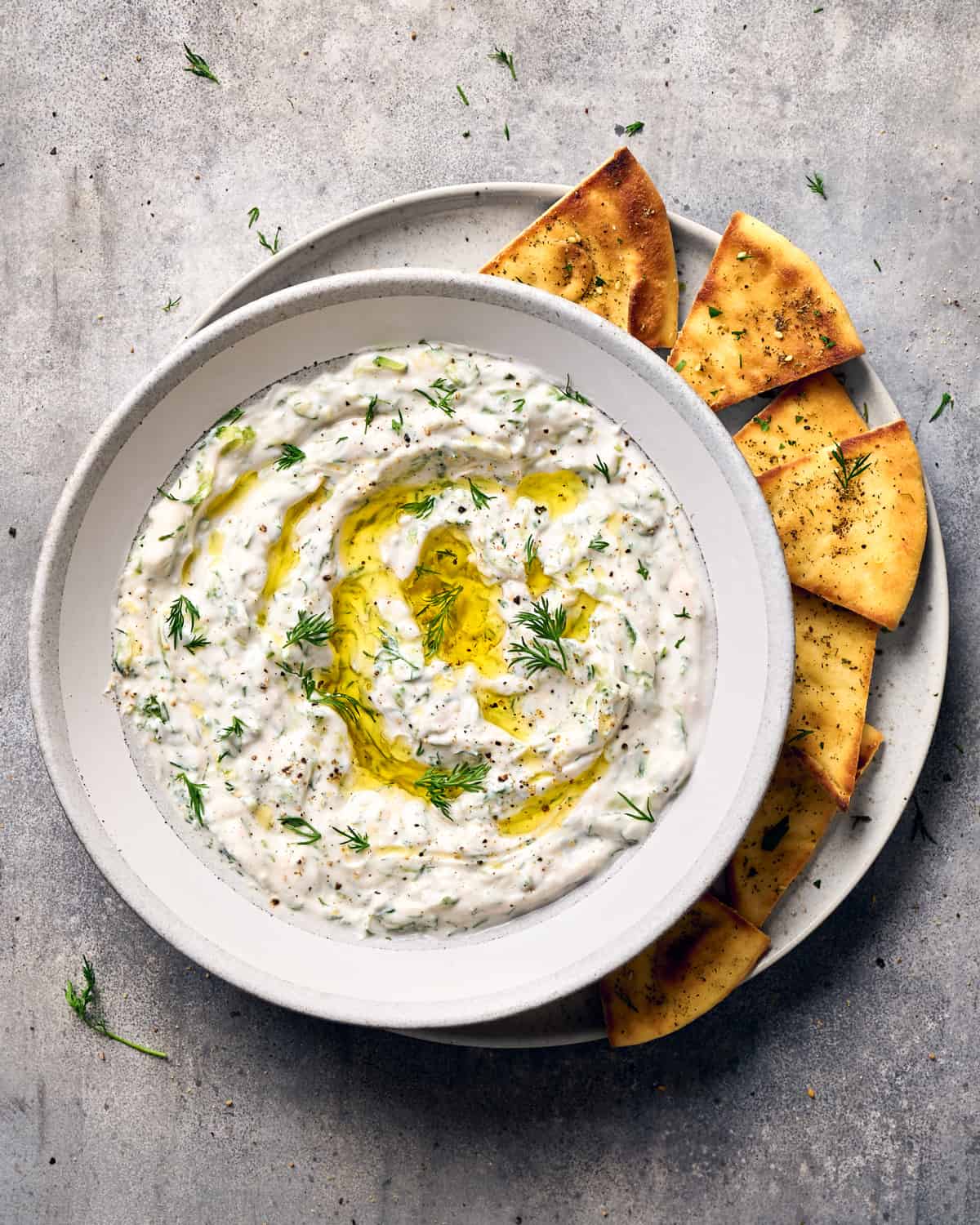Tzatziki in a bowl on a plate next to pita chips.