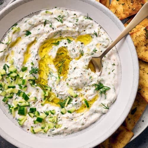 Closeup flatlay shot of vegan tzatziki in a bowl on a plate with pita chips.