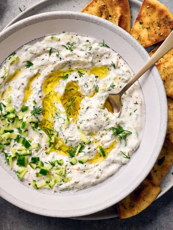 Closeup flatlay shot of vegan tzatziki in a bowl on a plate with pita chips.