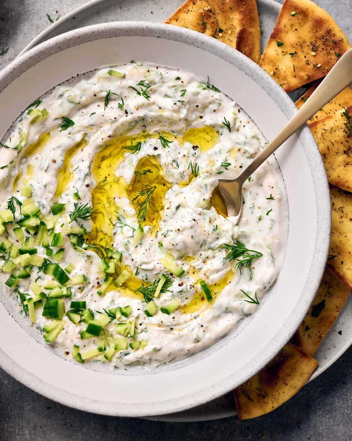Close up of tzatziki in a bowl on a plate with pita chips.