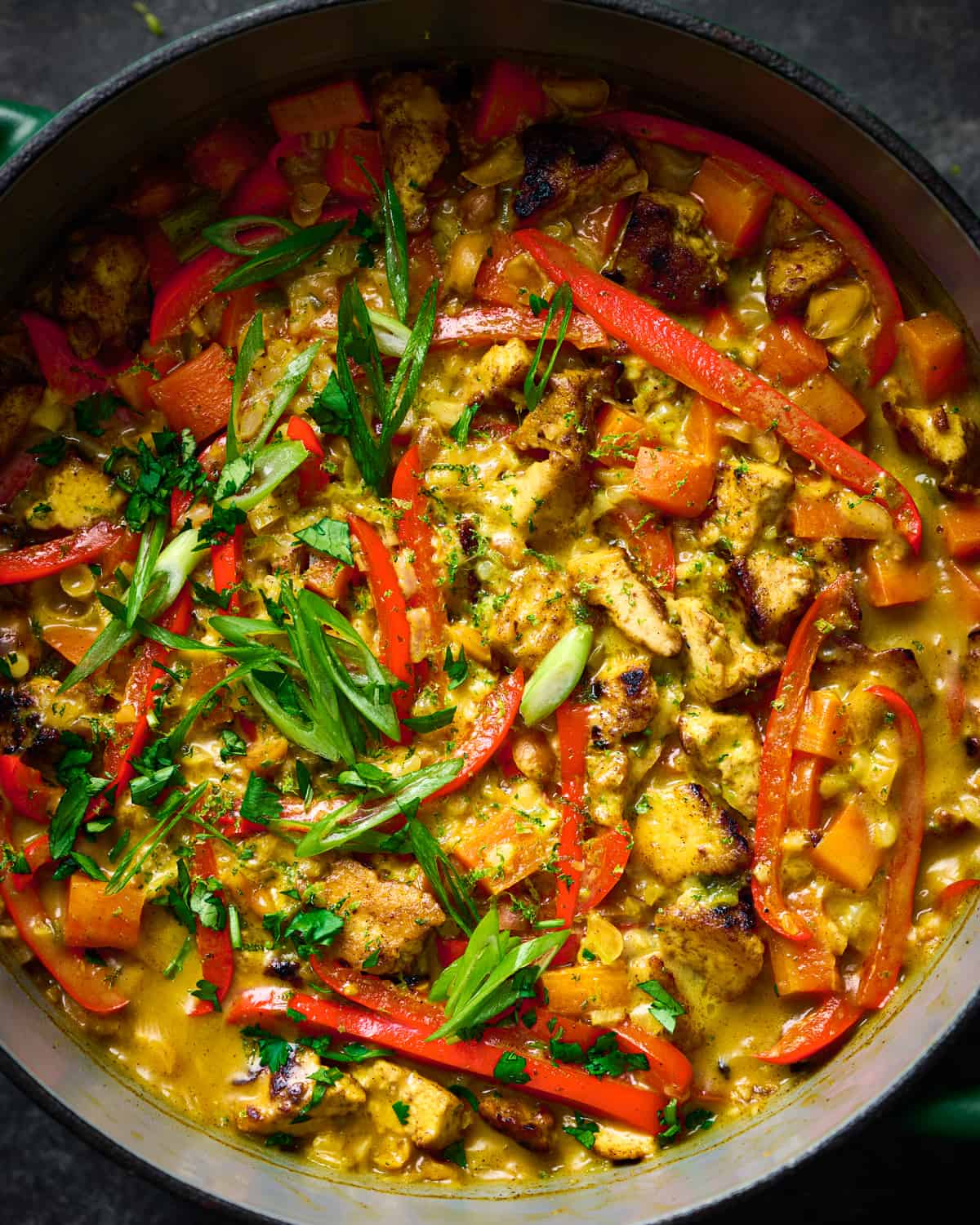 closeup shot of creamy rice and tofu with red bell peppers and scallions in a dutch oven.