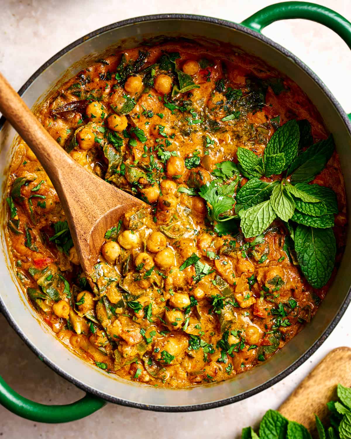 vegan chickpea curry in a green dutch oven garnished with mint and cilantro with a spoon dug in.