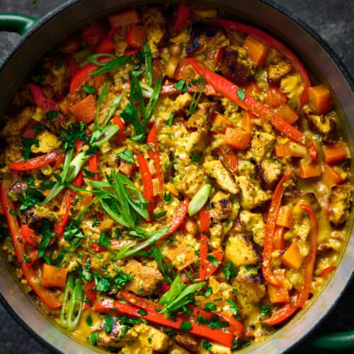 creamy golden rice and tofu with red bell peppers and scallions in a dutch oven.