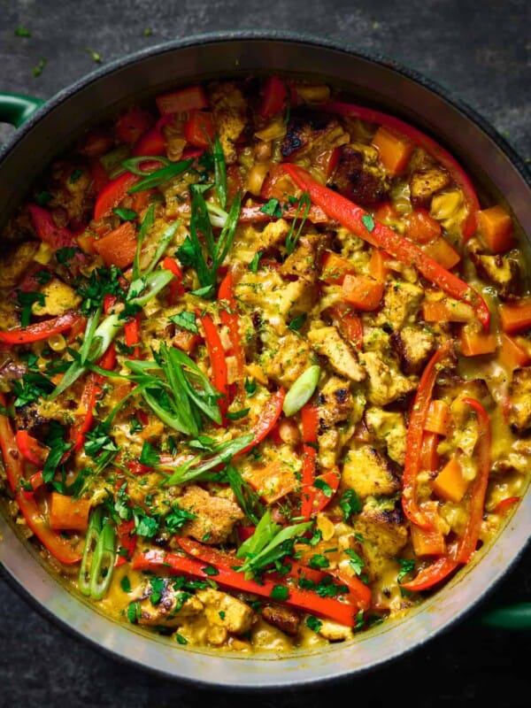 creamy golden rice and tofu with red bell peppers and scallions in a dutch oven.