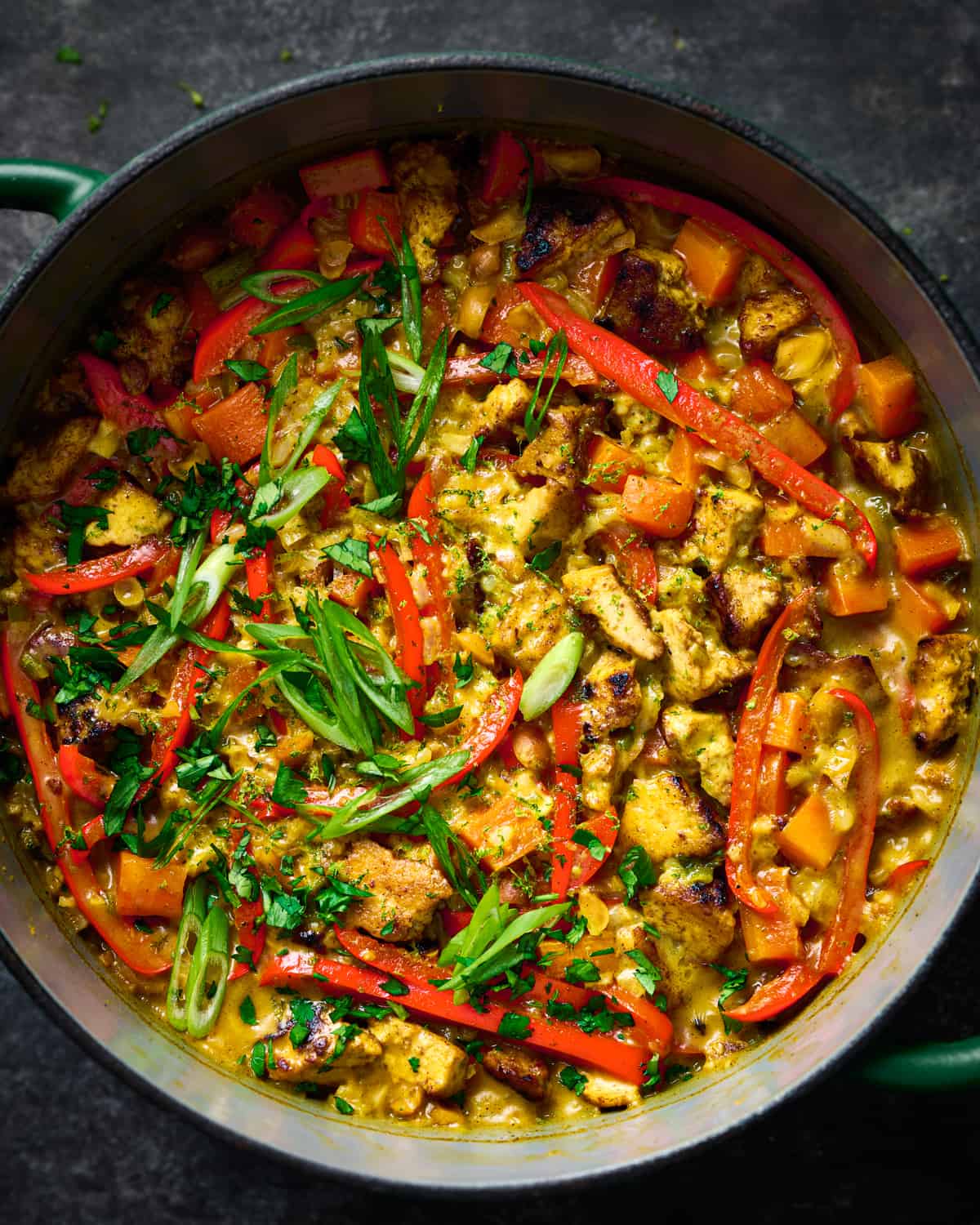 creamy golden rice and tofu with red bell peppers and scallions in a dutch oven.