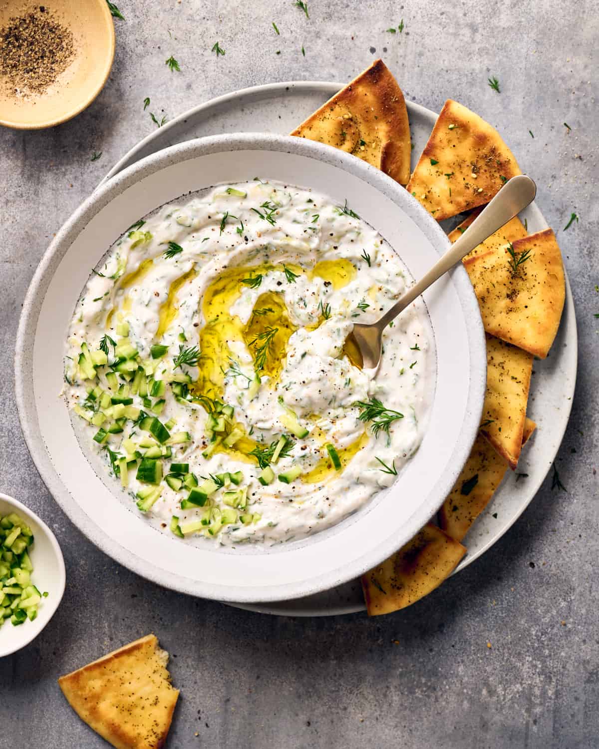 Overhead view of tzatziki in a bowl next to pita chips and small bowls with pepper and cucumber in them.