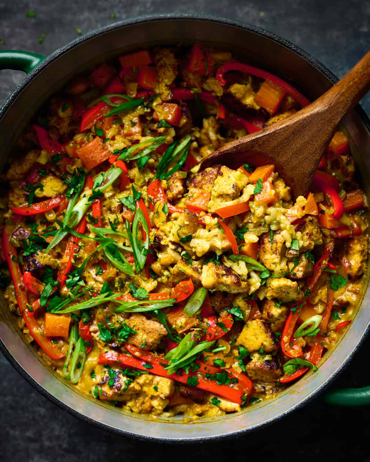 creamy golden rice and tofu with red bell peppers and scallions in a dutch oven with spoon dug in.