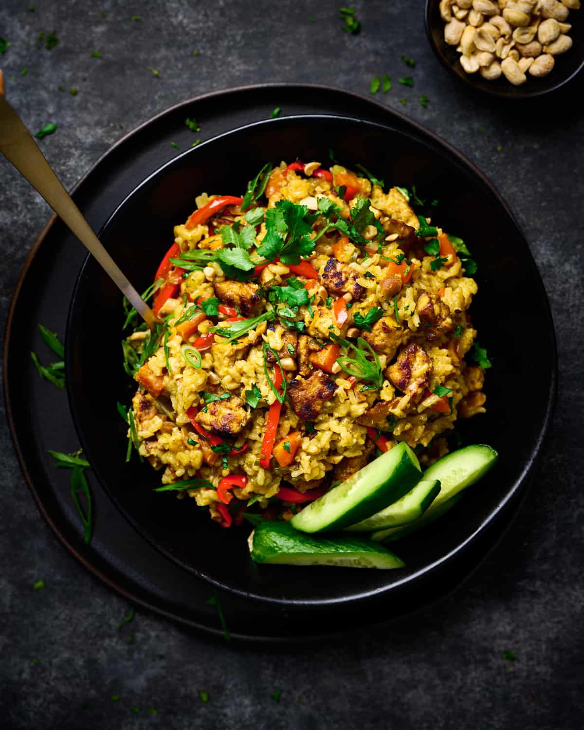 creamy golden rice with tofu and vegetables in a black bowl on a black plate.