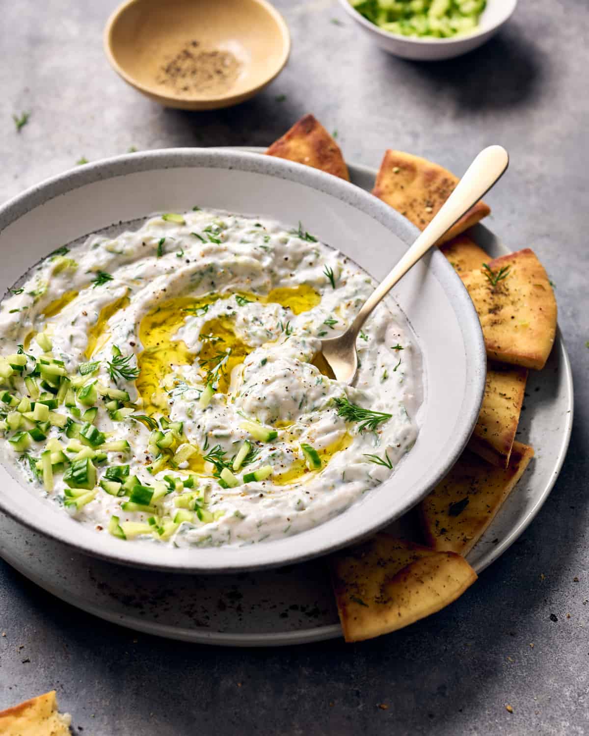 Side view of tzatziki in a bowl on a plate with pita chips.