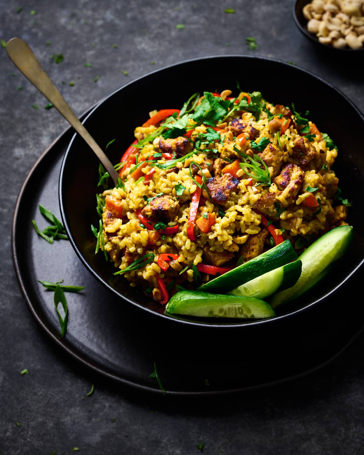 creamy golden rice with tofu and vegetables in a black bowl on a black plate.