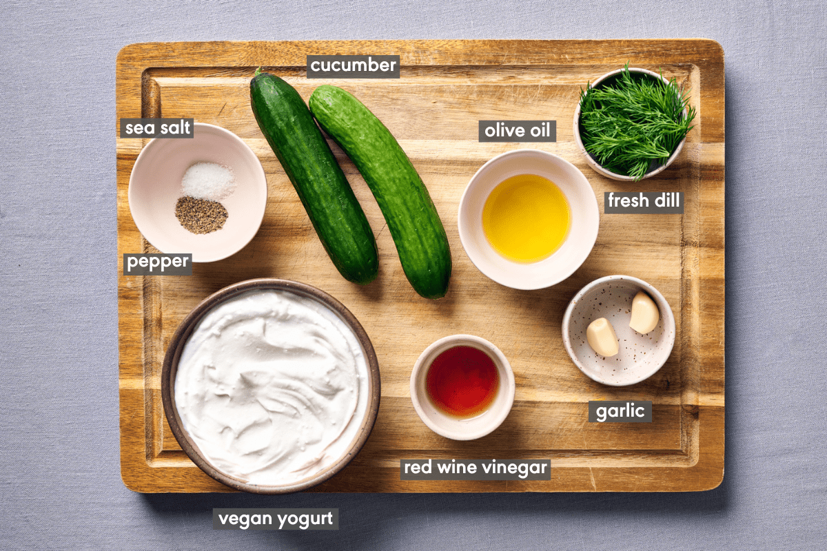 Tzatziki ingredients in various small bowls on a wooden cutting board.