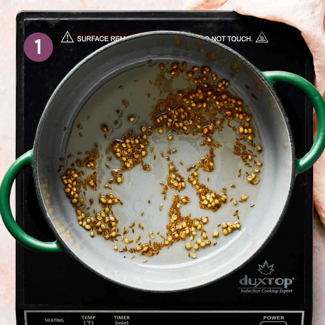 cumin and coriander seeds blooming in oil in a green dutch oven. 