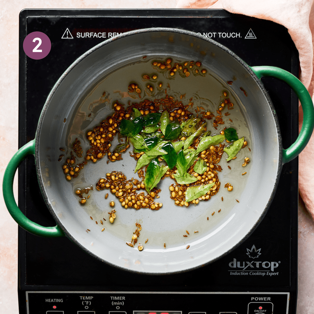 fresh curry leaves, cumin and coriander seeds blooming in oil in a green dutch oven. 