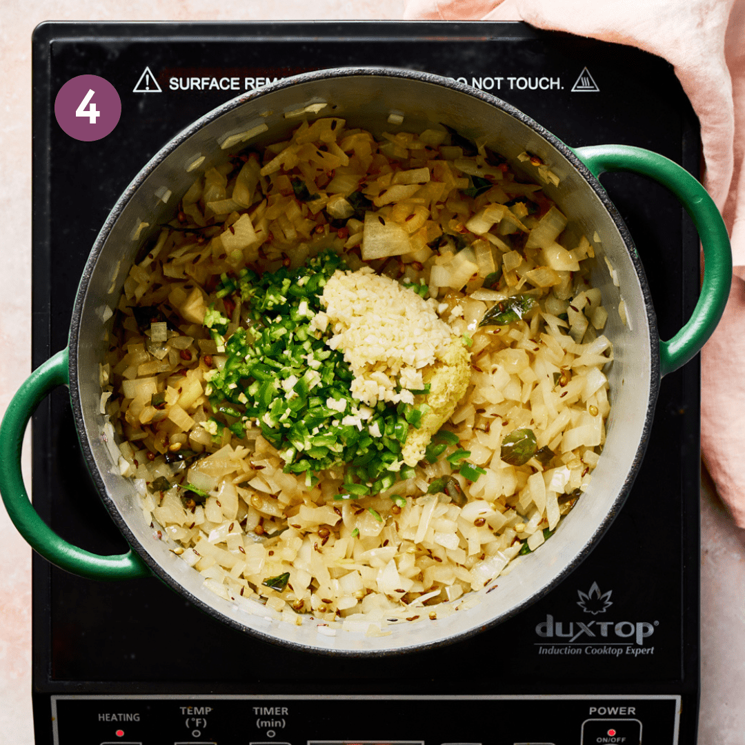 garlic, ginger, and green chili peppers on top of sauteed onions in a green Dutch oven.