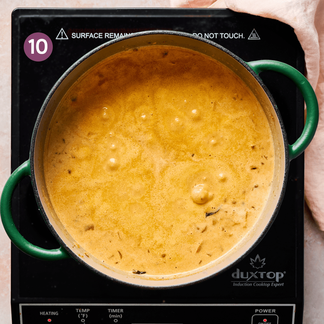 creamy vegan curry in a light orange color simmering in a green dutch oven.