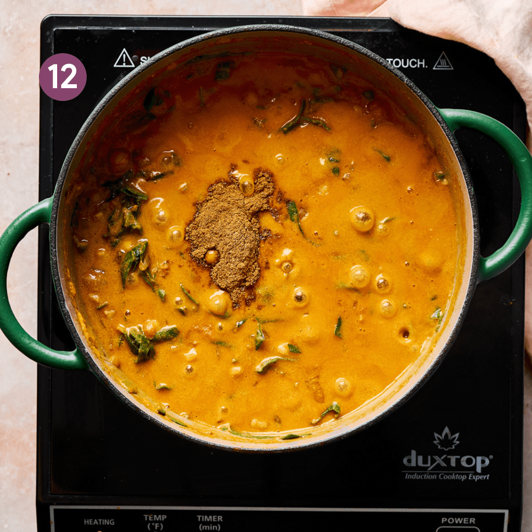 vegan Indian chickpea curry simmering in a green dutch oven with garam masala on top.