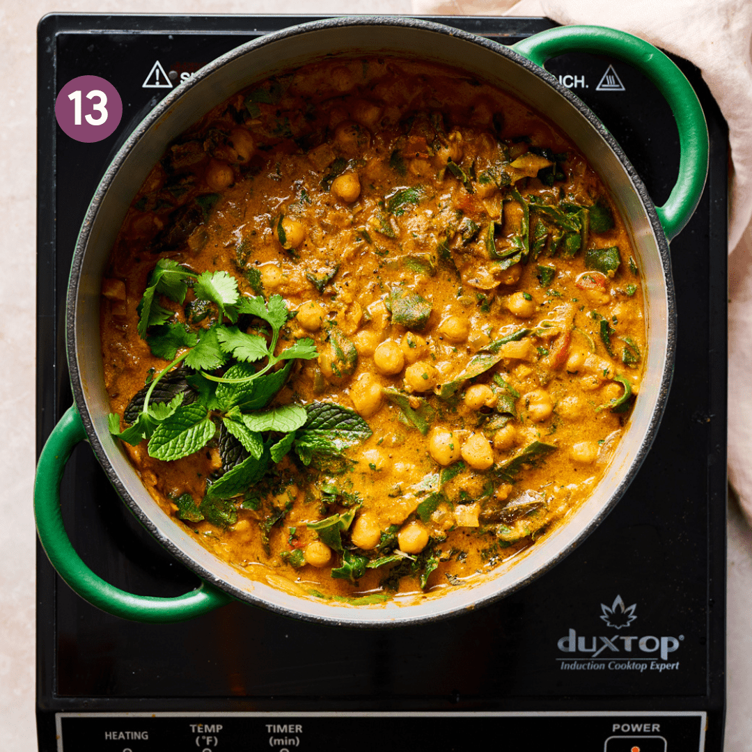 vegan chickpea curry in a green dutch oven garnished with fresh mint and cilantro.