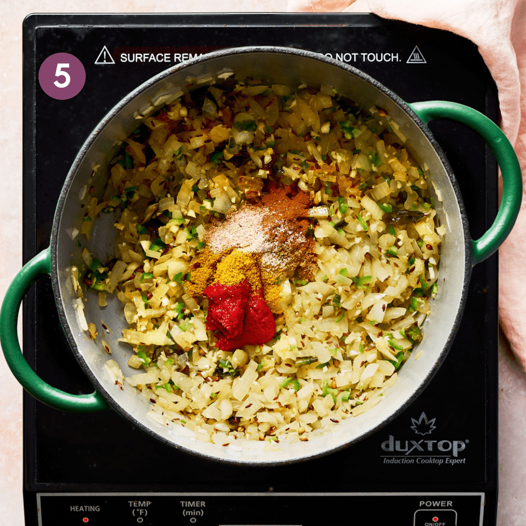 Indian spices and tomato paste on top of sauteed onions and garlic in a green Dutch oven.