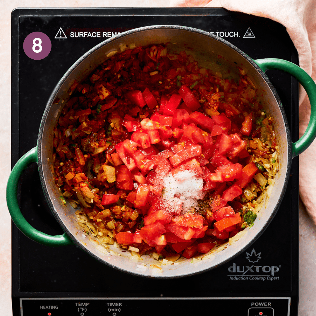 diced tomatoes and salt sitting on top of an Indian spiced masala in a green Dutch oven.