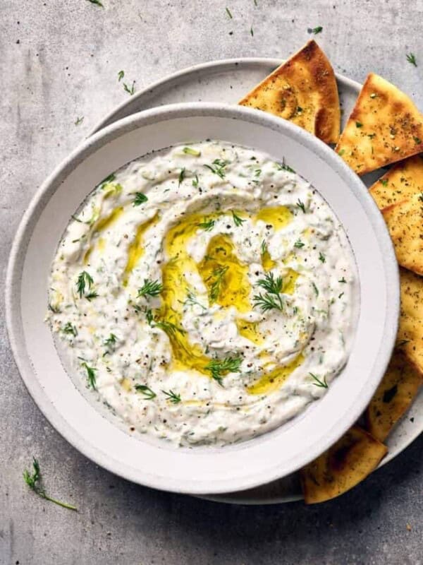 Tzatziki in a bowl on a plate next to pita chips.