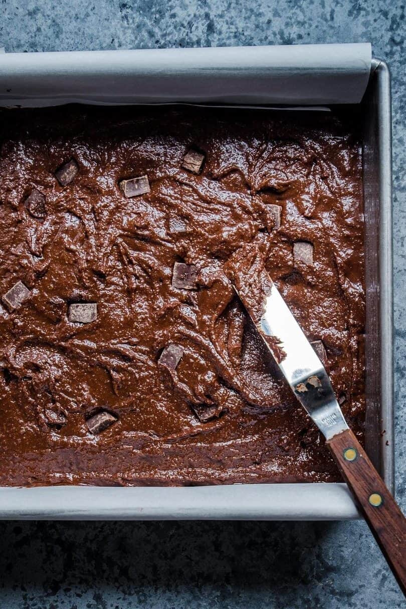 Brownie batter with chocolate chunks in a square baking tin