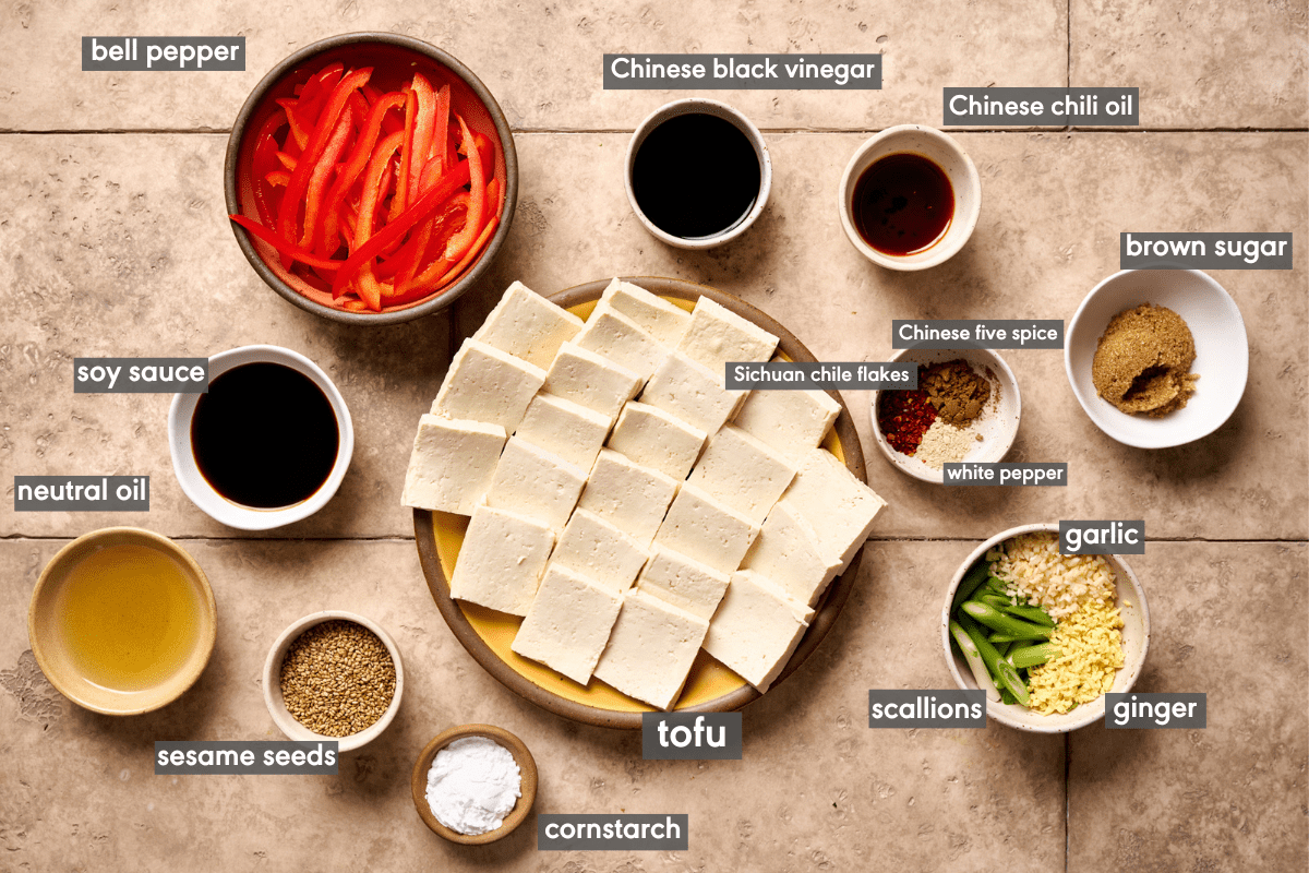 Braised tofu ingredients in various sized bowls on a tan table.
