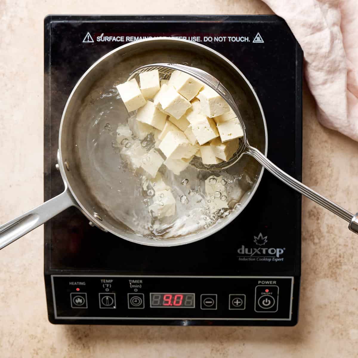 person adding tofu to a pot of boiling water using a spider tool.