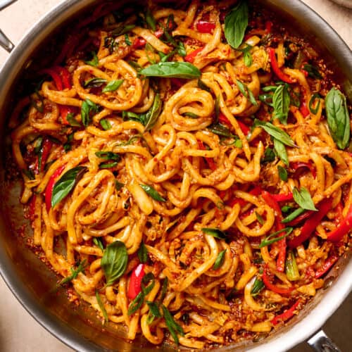 gochujang noodles in a saute pan, garnished with thai basil on a tan table.