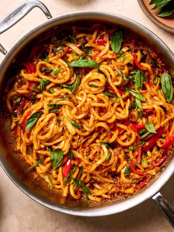 gochujang noodles in a saute pan, garnished with thai basil on a tan table.