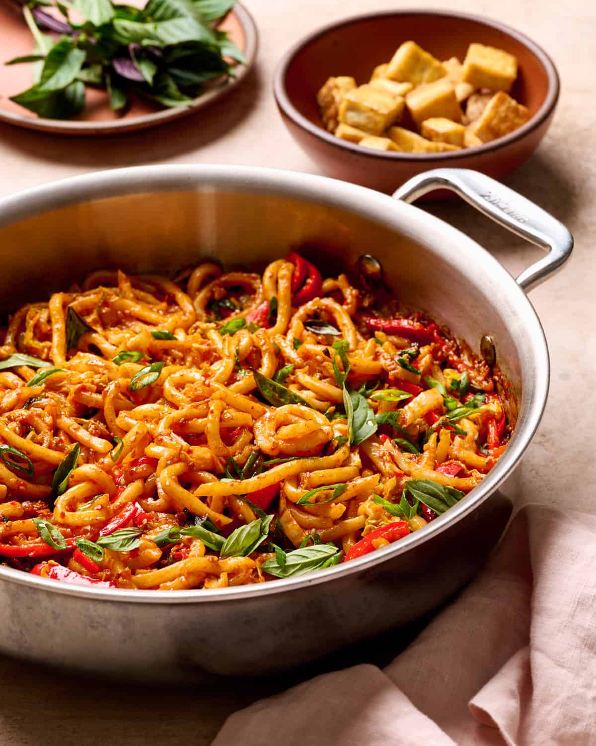 Backlit view of gochujang noodles in a saucepan on a tan table.