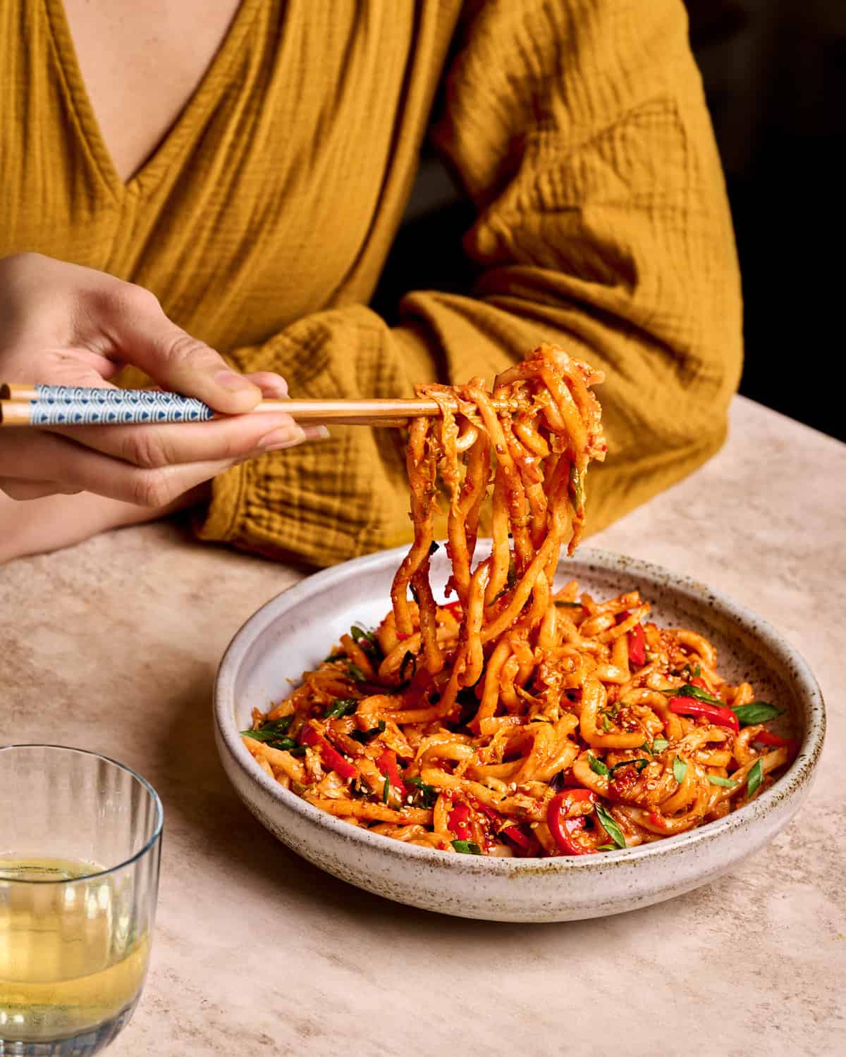 Woman sitting at a table eating gochujang noodles from a bowl with chopsticks.