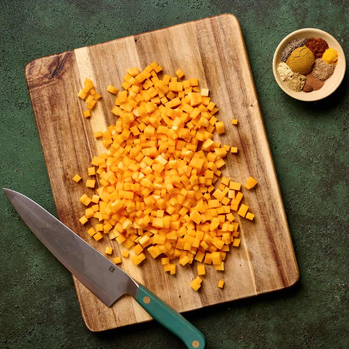 Small chopped butternut squash pieces on a wooden cutting board with a knife.