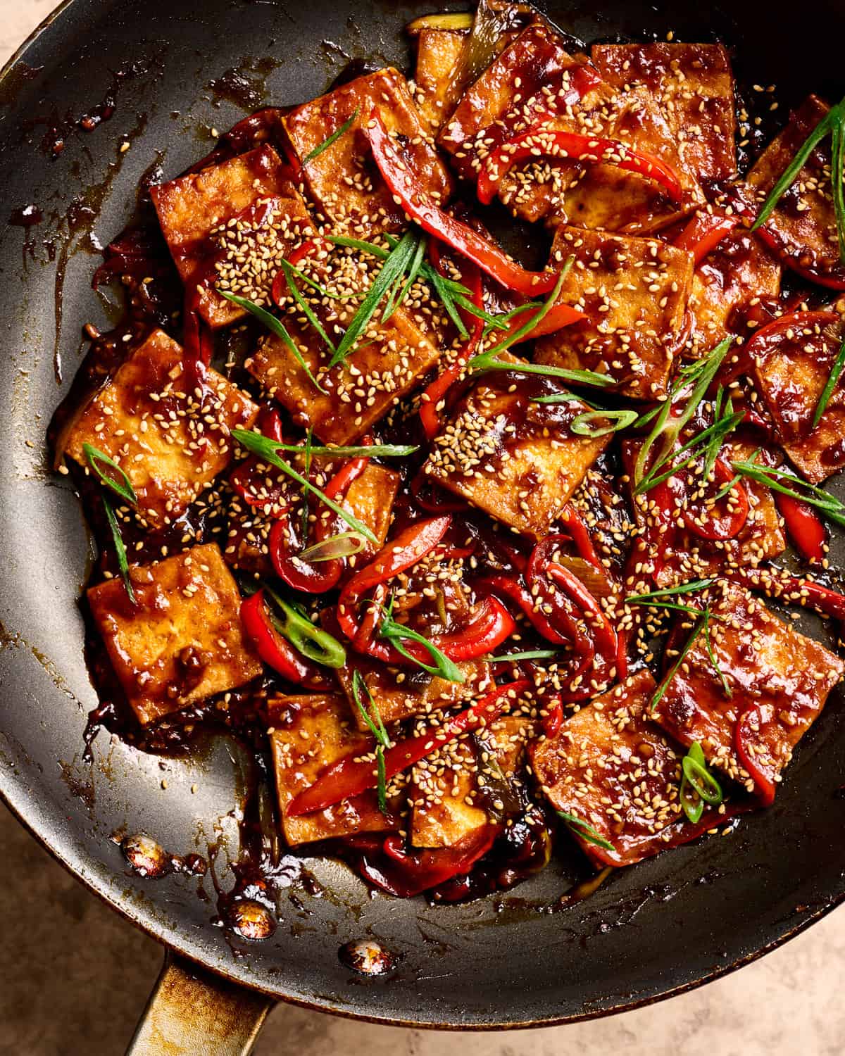 Close up of finished braised tofu dish in a black wok on a tan table.