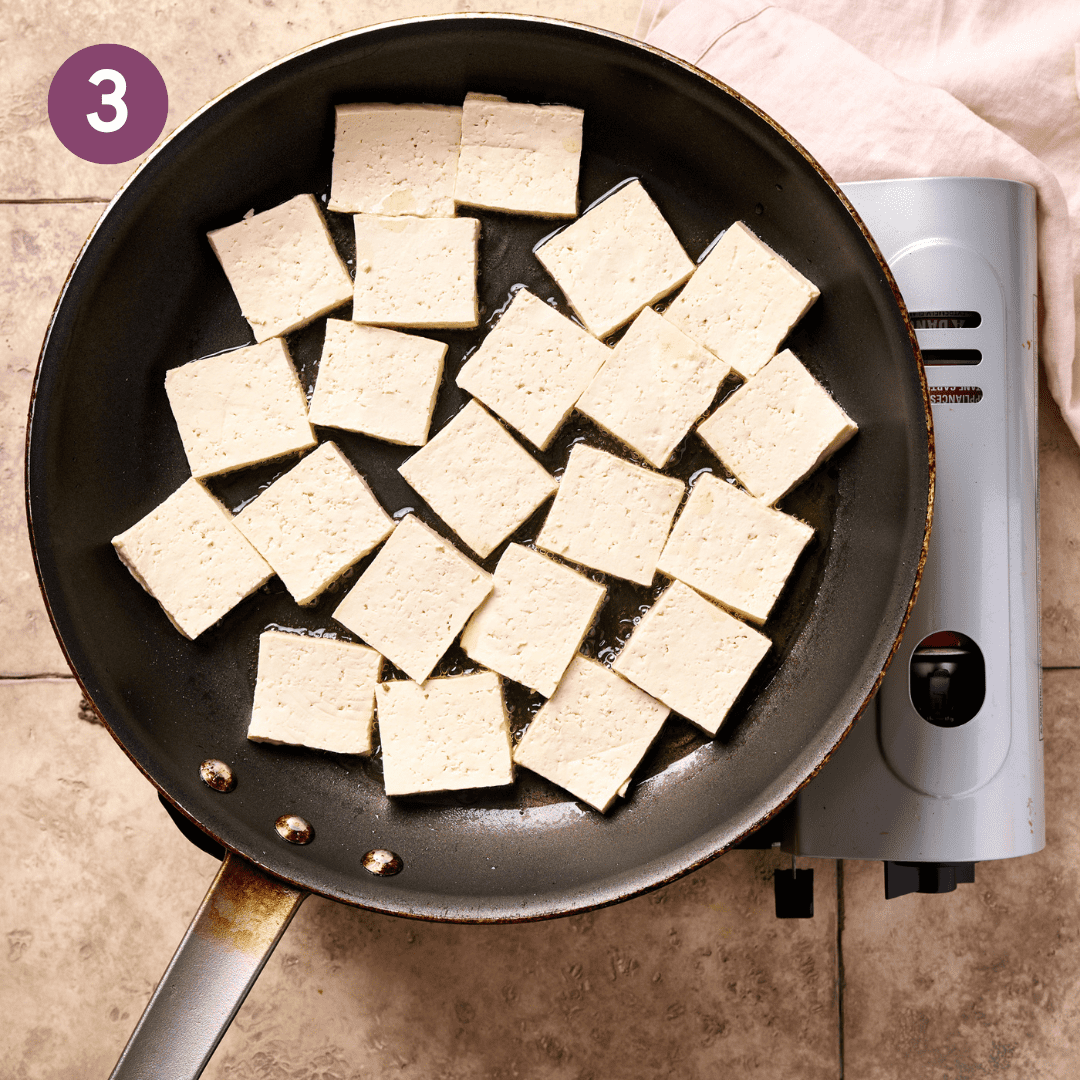 Tofu frying in oil in the pan.