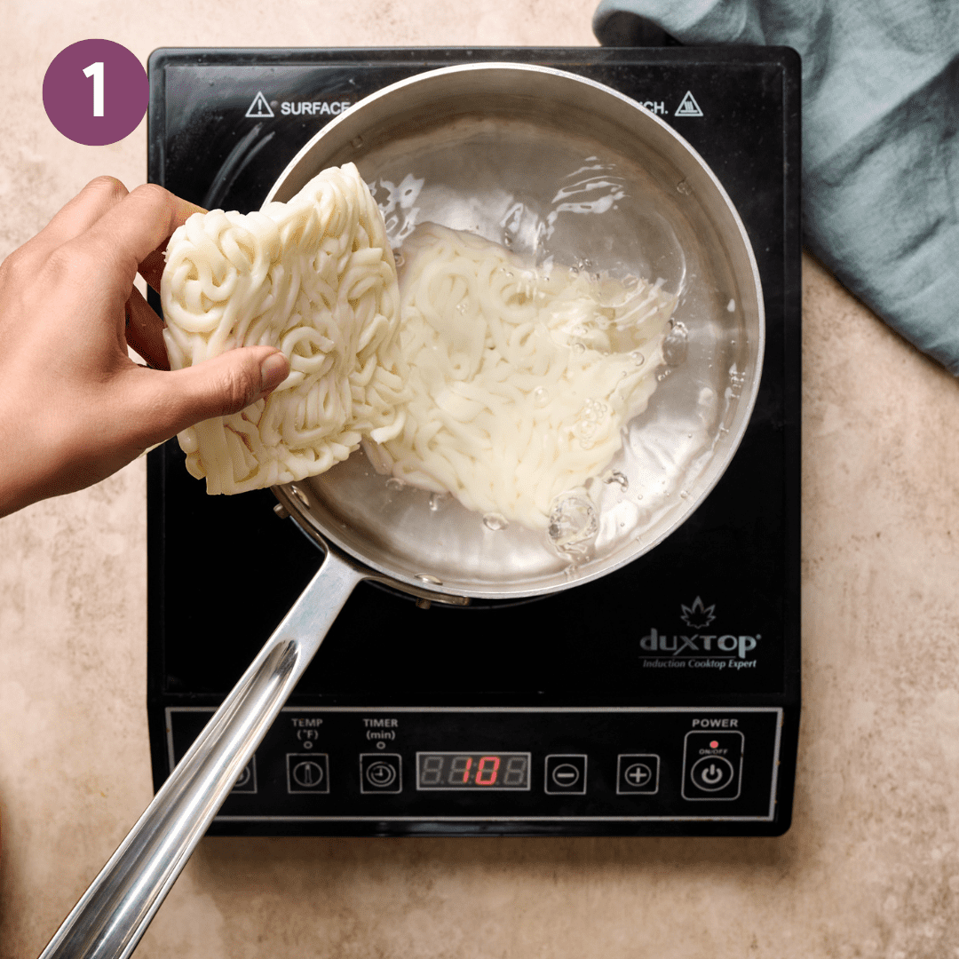 Person adding fresh udon noodles into a saucepan with boiling water.