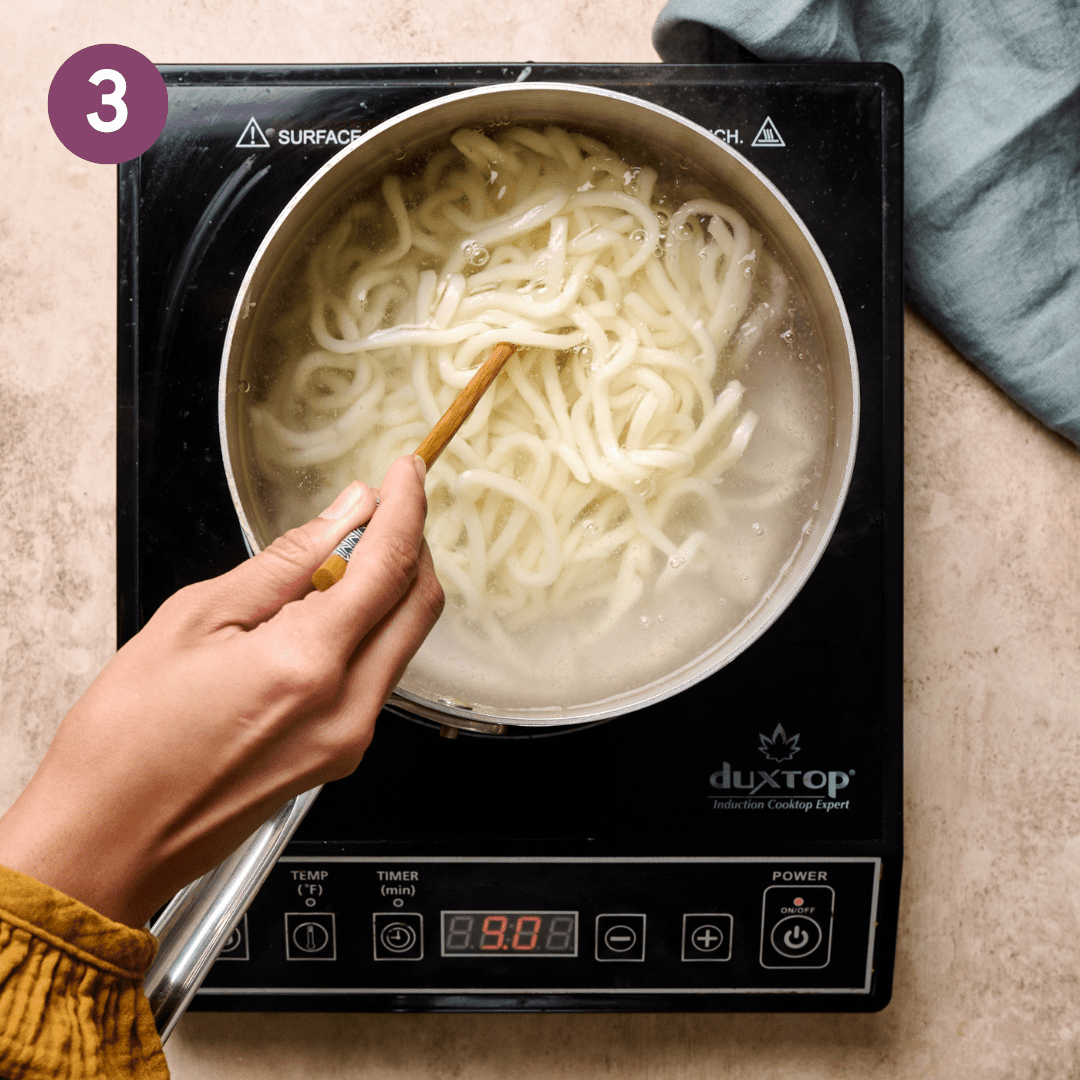 Person using chopsticks to separate stuck udon noodles in boiling water.