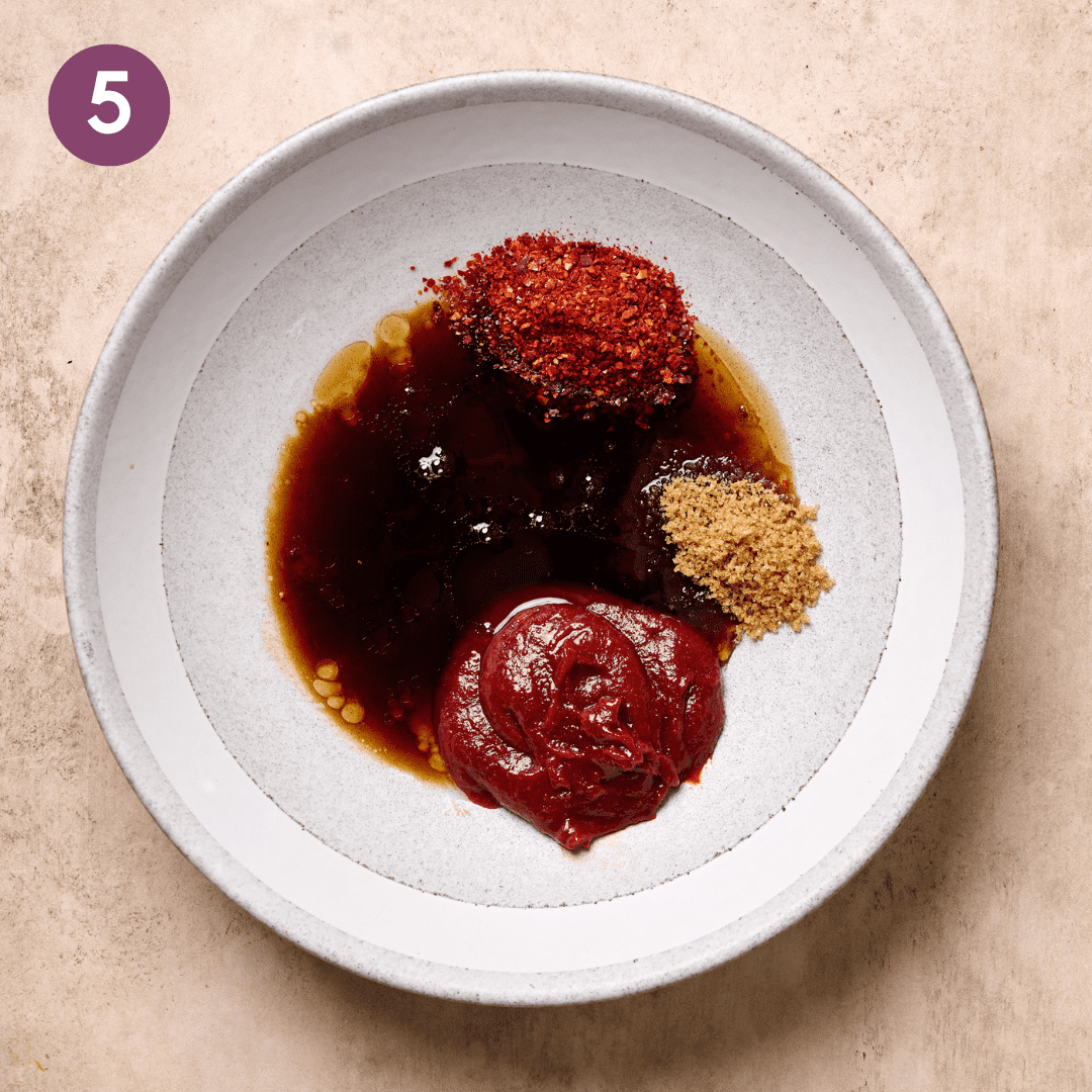 Gochujang sauce ingredients in a white bowl on a tan table.