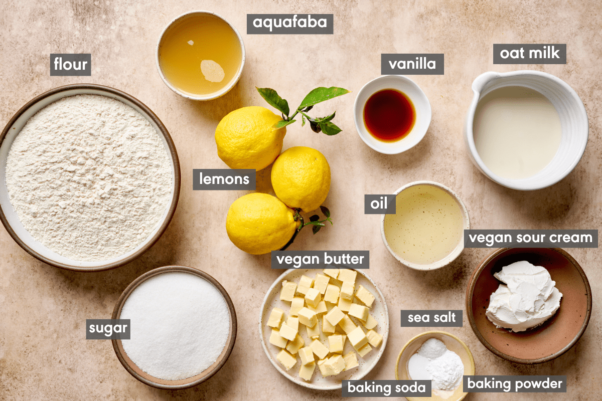 ingredients for vegan lemon cake laid out on a light pink surface with ingredients labeled. 