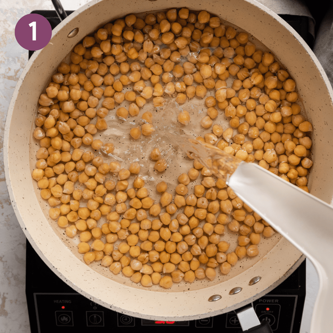 Person pouring water into a saucepan with chickpeas.