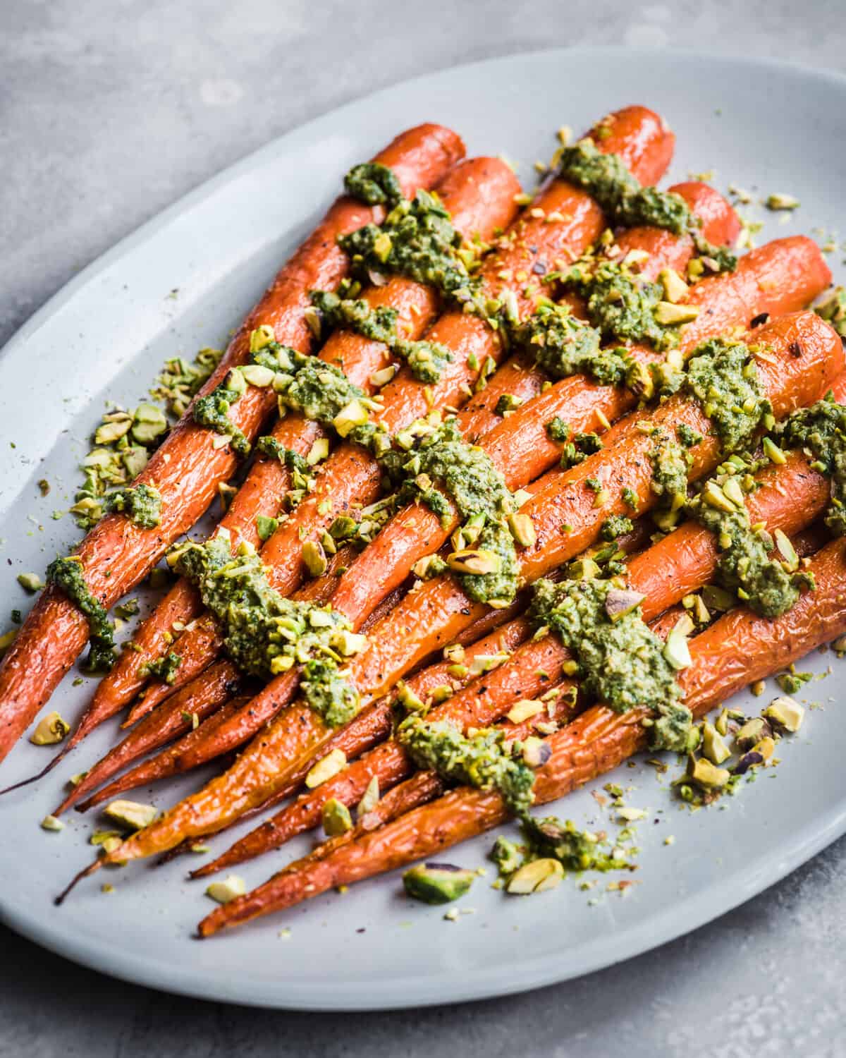 Carrots covered in carrot top pesto on a white platter on a grey table.